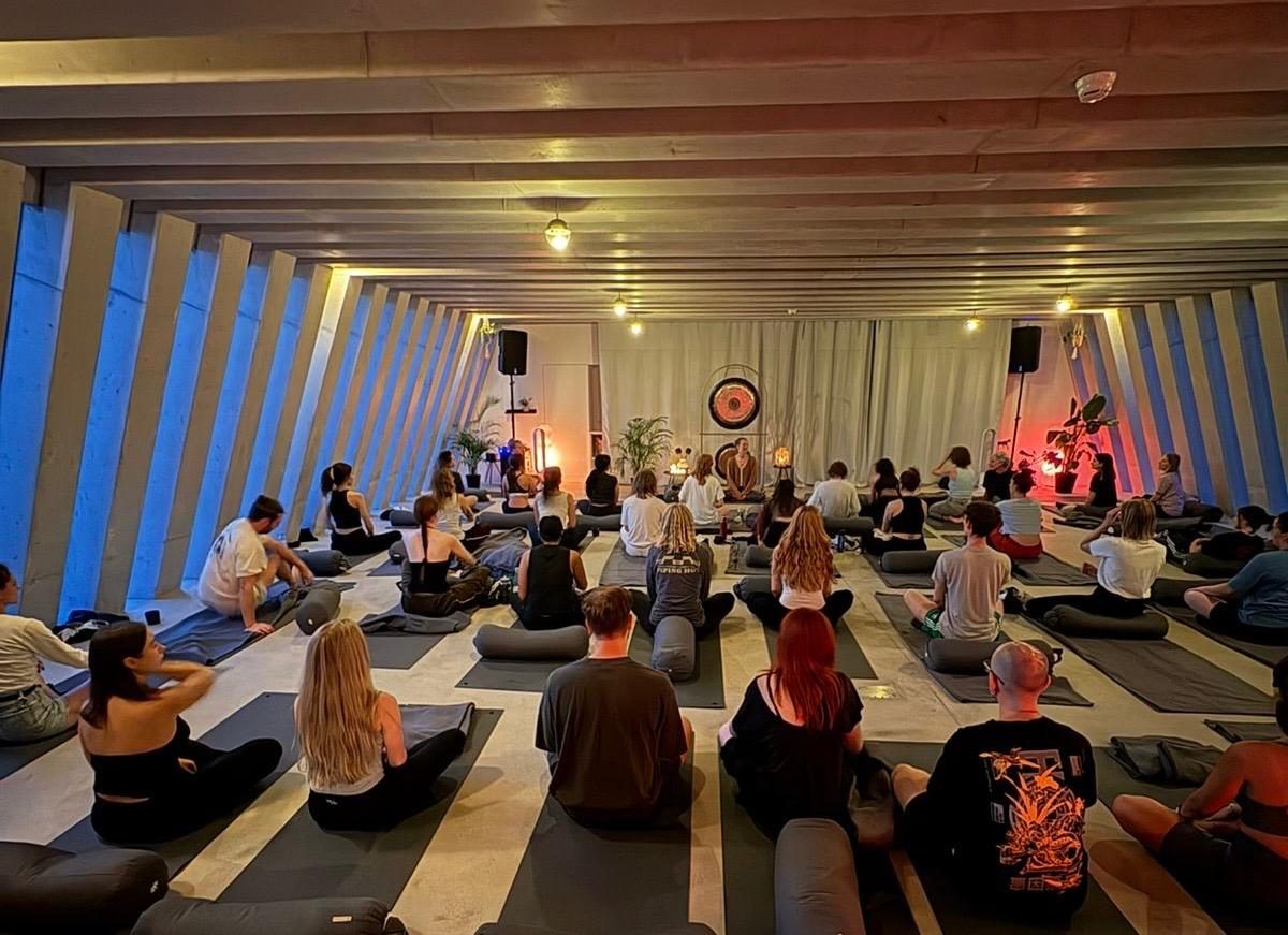 Group class seated on mats facing Leda and a gong in a candlelit studio